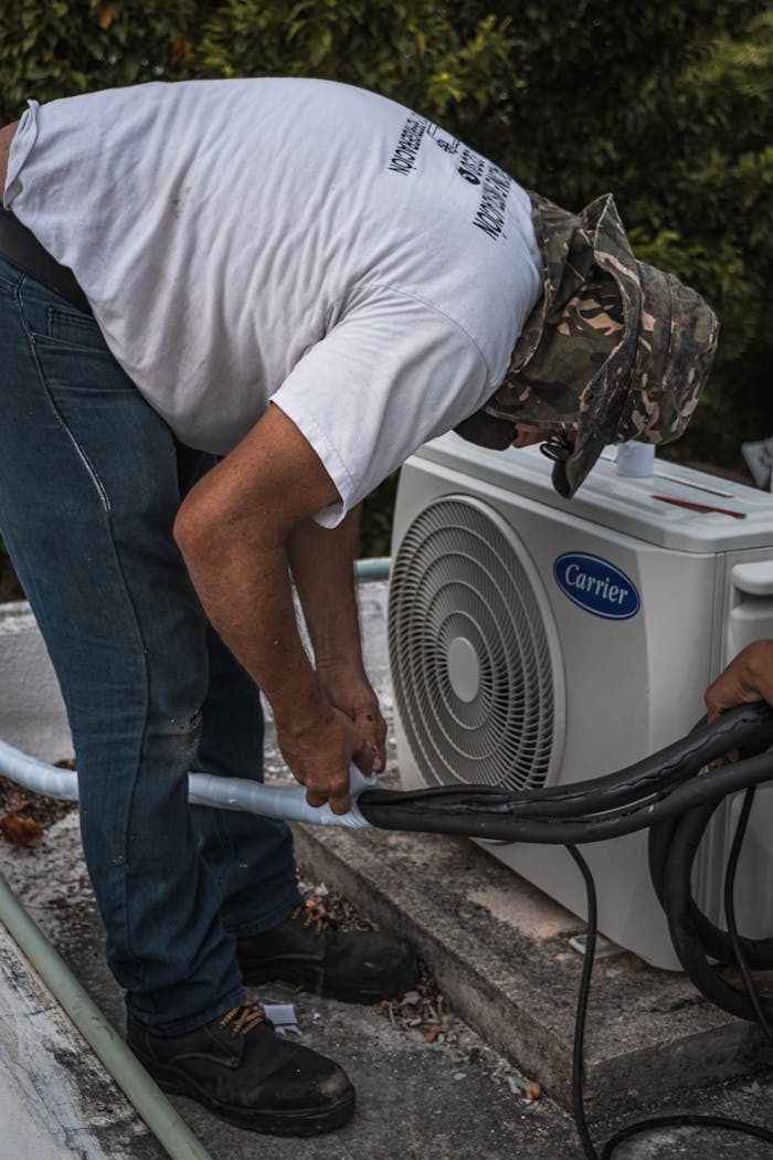 our-experience A technician performs maintenance on an outdoor air conditioning unit, focusing on hose connections.